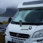 Récit de voyage en islande en camping-car : camping-car blanc sur aire près d’un fjord, météo froide et route humide