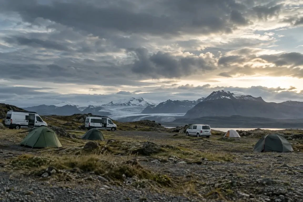 Camping Höfn Islande avec vans, tentes et montagnes glaciaires en arrière-plan